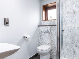 A bathroom with a toilet, toilet paper holder, sink, small window, and a shower with marble-patterned walls at Glentress Forest White Willow Premium in Glentress Forest Peebles