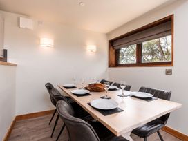 A dining room with a wooden table set with plates and glasses surrounded by black chairs and a window in Glentress Forest White Willow Premium Glentress Forest Peebles