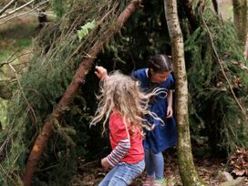 Two children playing in a shelter made of tree branches and leaves in a forest
