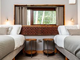 A bedroom with two single beds separated by two round wooden bedside tables and a window showing trees at Glentress Forest White Willow Premium Valley View Glentress Forest Peebles