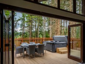 An outdoor deck with a dining table set and hot tub surrounded by trees at Glentress Forest White Willow Premium Valley View in Glentress Forest Peebles