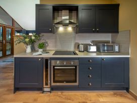 A kitchen with dark cabinets an electric stove an oven toaster kettle microwave flowers and an open book on the counter at Garwnant Golden Oak Hideaway in Garwnant Bannau Brycheiniog Brecon Beacons
