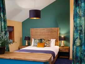 A bedroom with a wooden bed frame blue and floral pillows wooden nightstands with lamps and floral curtains at Glentress Forest Golden Oak Hideaway Glentress Forest Peebles