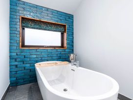 A bathroom with a white freestanding bathtub in front of a blue tiled wall with a window at Glentress Forest Golden Oak Hideaway in Glentress Forest Peebles