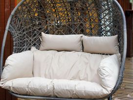 A woven hanging chair with beige cushions on a wooden deck at Glentress Forest Golden Oak Hideaway Glentress Forest Peebles
