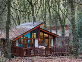 A wooden cabin with large windows and a fenced porch in a forest setting at Glentress Forest Golden Oak Hideaway Glentress Forest Peebles