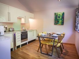 A kitchen with white cabinets a dining table with yellow chairs and tableware and a painting on the wall at Beddgelert Golden Oak - freshly inspired design Beddgelert Eryri Snowdonia