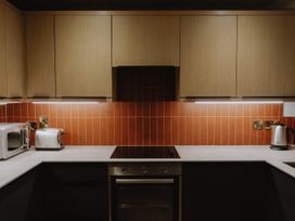 A kitchen with wood cabinets red tiled backsplash microwave toaster stovetop oven and electric kettle at Glentress The Unfurl Cabin 2 Bed Glentress Forest Peebles