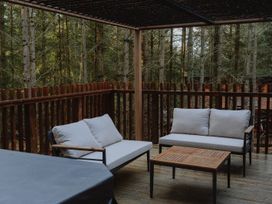 An outdoor wooden deck with two cushioned sofas and a wooden coffee table surrounded by trees at Glentress The Unfurl Cabin (2 Bed) Glentress Forest Peebles