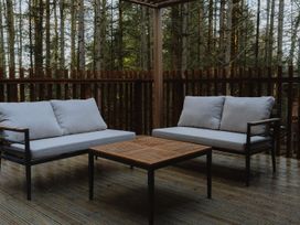 An outdoor seating area with two sofas and a wooden table on a deck surrounded by trees at Glentress The Unfurl Cabin (2 Bed) Glentress Forest Peebles