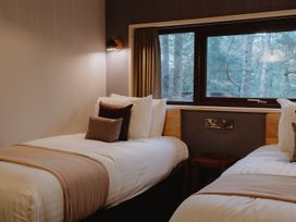 A bedroom with two single beds with pillows and blankets and a window showing trees outside at Glentress The Unfurl Cabin 2 Bed in Glentress Forest Peebles