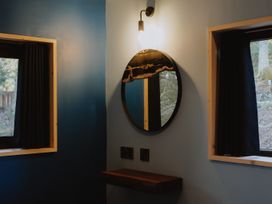 A corner of a room with a circular mirror under a wall light between two windows with black curtains at Glentress The Unfurl Cabin (2 Bed) in Glentress Forest Peebles