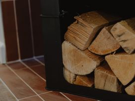 A stack of firewood in a black metal holder on a tiled floor at Glentress The Unfurl Cabin (2 Bed) Glentress Forest Peebles