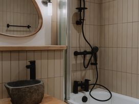 A bathroom with a stone sink a wooden countertop a mirror a bathtub and black shower fixtures at Glentress The Unfurl Cabin (2 Bed) Glentress Forest Peebles