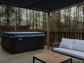 A covered outdoor deck with a hot tub sofa and wooden table surrounded by trees at Glentress The Unfurl Cabin 4 Bed in Glentress Forest Peebles