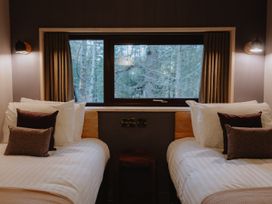 A bedroom with two single beds and a window showing trees at Glentress The Unfurl Cabin (4 Bed) in Glentress Forest Peebles