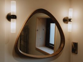 A triangular wooden framed mirror on a wall with two wall lights and a window reflection at Glentress The Unfurl Cabin (4 Bed) Glentress Forest Peebles