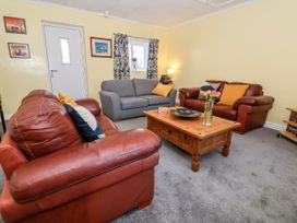 A living room with two brown leather sofas and one gray fabric sofa around a wooden coffee table with flowers at Millers Cottage in Old Malton near Malton