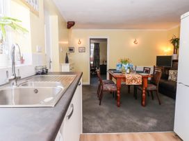 A kitchen sink area leading into a dining room with a wooden table set for four and a living area with a sofa and television at Millers Cottage Old Malton near Malton