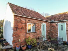 An outdoor patio area with potted plants metal table and chairs outside brick buildings with green doors at Millers Cottage Old Malton near Malton