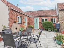 A patio with a glass table and four chairs in front of a brick building with green doors and windows at Millers Cottage Old Malton near Malton