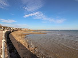 A curved sea wall with a sandy beach and houses along the shoreline at Seaward in Rhos-On-Sea