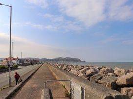 A coastal walkway and road with houses on one side and rocks along the shore on the other at Seaward in Rhos On Sea