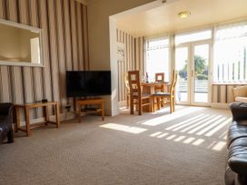 A living room with a television on a wooden stand a dining table with chairs and striped wallpaper at Seaward in Rhos-On-Sea