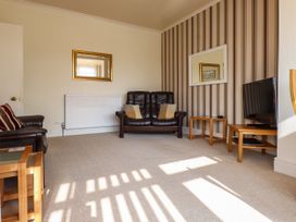 A living room with two brown leather sofas a television on a wooden stand and two mirrors at Seaward in Rhos-On-Sea