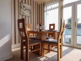 A dining area with a round wooden table set for four with wine glasses and a bottle of wine near glass doors at Seaward in Rhos-On-Sea