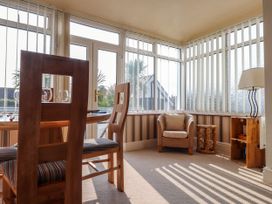 A dining area with wooden chairs and table next to a wicker armchair and small wooden shelf with a lamp at Seaward in Rhos-On-Sea