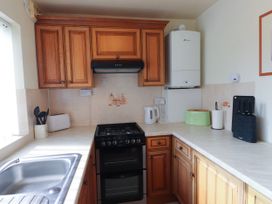 A kitchen with wooden cabinets a gas stove a white kettle a green toaster a knife block and a sink at Seaward in Rhos-On-Sea