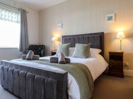 A bedroom with a grey upholstered bed two bedside tables with lamps and a green armchair by the window at Seaward in Rhos-On-Sea