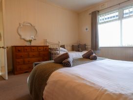 A bedroom with a double bed with rolled towels and a green runner a wooden dresser with a mirror and a white metal daybed near a window at Seaward in Rhos-On-Sea