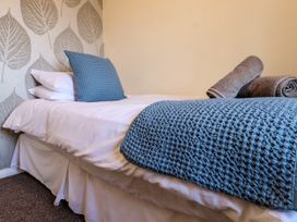 A bedroom with a bed with white sheets blue pillow and blanket and rolled towels at Seaward in Rhos On Sea