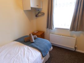 A small bedroom with a single bed covered in white and blue linens two rolled towels on the bed a wooden nightstand a window with curtains a radiator and a wall-mounted cabinet at Seaward Rhos-On-Sea