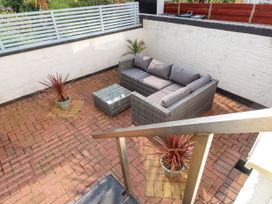 An outdoor patio with a wicker sofa with cushions a glass-top coffee table and two potted plants surrounded by white walls