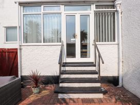Exterior view of a house entrance with four black steps leading to a white door flanked by large windows with vertical blinds at Seaward in Rhos-On-Sea