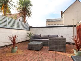 An outdoor patio with a gray sofa, a matching coffee table, potted plants, and white walls at Seaward in Rhos-On-Sea