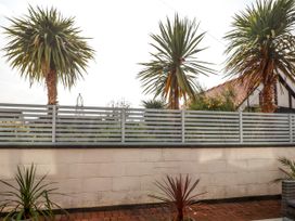 An outdoor area with a brick floor potted plants a white wall and palm trees behind a slatted fence at Seaward in Rhos-On-Sea