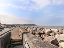 A coastal road with houses on one side and large rocks forming a seawall on the other side at Seaward in Rhos-On-Sea