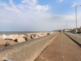 A coastal walkway next to a sea wall with rocks and a row of houses along a road at Seaward in Rhos On Sea