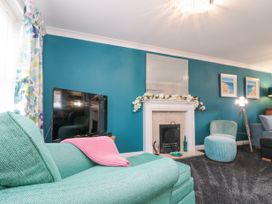 A living room with teal walls a fireplace with flowers a teal sofa and chair a television and framed paintings at 48 Aysgarth Rise Bridlington