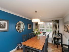A dining room with a wooden table and eight chairs a vase of flowers on the table a blue accent wall with a mirror and framed photos curtains with leaf patterns a window and two hanging lights at 48 Aysgarth Rise Bridlington