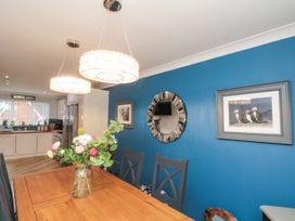 A dining area with a wooden table and chairs a glass vase with flowers blue wall with a round decorative mirror and framed picture a kitchen with white cabinets in the background at 48 Aysgarth Rise Bridlington