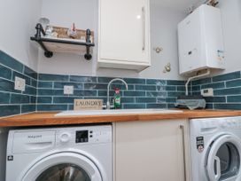 A laundry room with a washing machine and dryer under a wooden countertop with a sink and blue tiled backsplash at 48 Aysgarth Rise Bridlington
