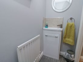 A small bathroom corner with a white sink cabinet a round mirror a green towel a radiator and a small trash bin at 48 Aysgarth Rise Bridlington