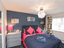 A bedroom with a bed with blue and pink bedding two gray dressers with lamps and decorations a window with curtains and pictures on a blue wall at 48 Aysgarth Rise in Bridlington