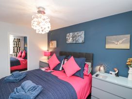 A bedroom with a bed with dark and pink bedding blue towels on it blue accent wall with bird paintings bedside tables with lamps and decorations at 48 Aysgarth Rise in Bridlington