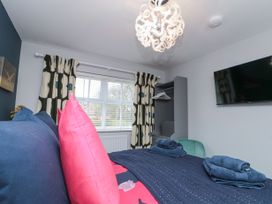 A bedroom with a bed with blue and pink pillows a TV on the wall and a window with patterned curtains at 48 Aysgarth Rise Bridlington
